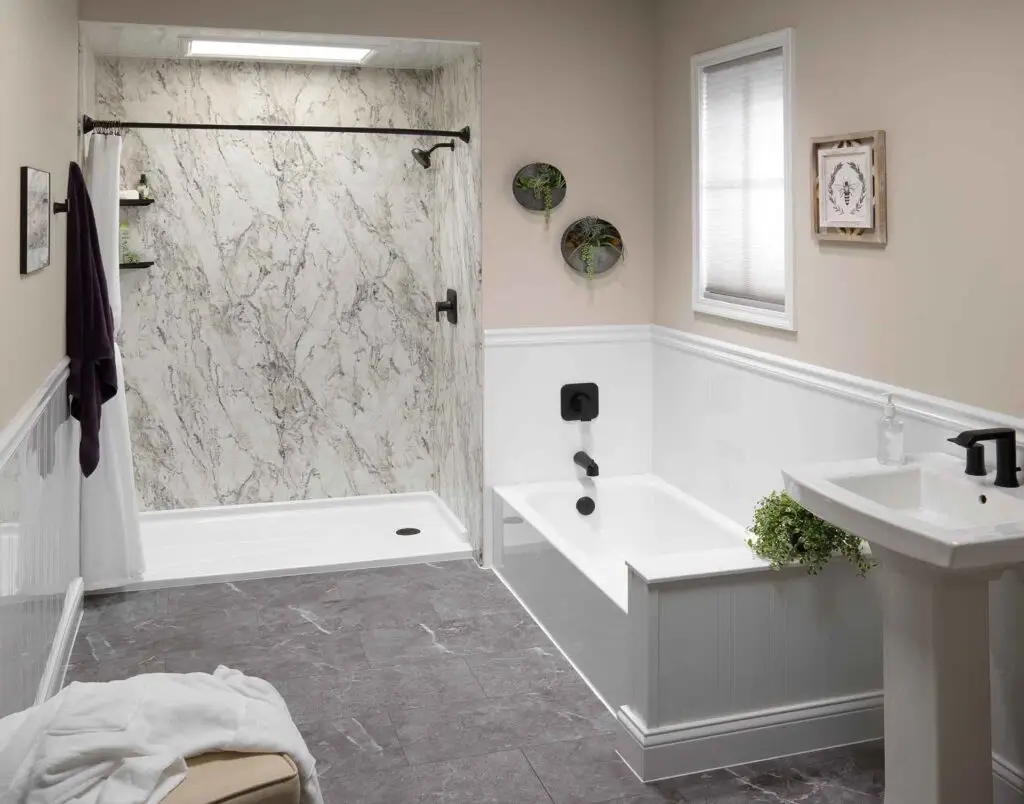 Modern bathroom with marble shower walls, a white tub, and matte black fixtures; gray tile floor and a window with blinds.