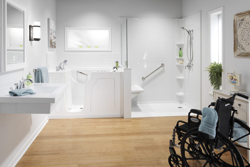 Bright accessible bathroom with a walk-in shower on the right, a white bathtub with grab bars in the center, and two black wheelchairs with teal towels in the foreground.