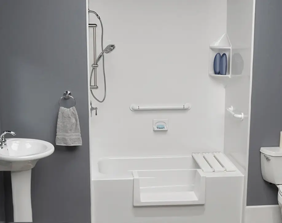 Accessible bathroom featuring a white tub with a built‑in seat, grab bar, and handheld shower; sink and toilet nearby for accessibility access.