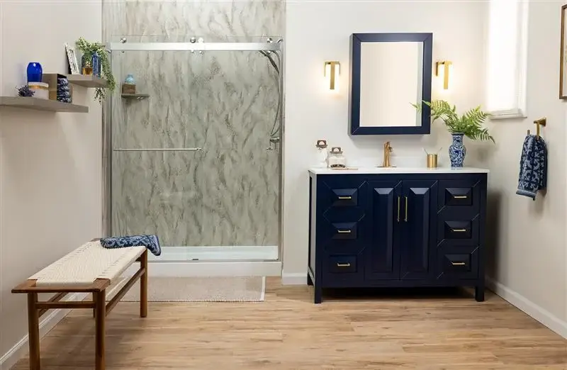 Blue bathroom vanity with gold hardware and a matching framed mirror beside a glass shower with marble walls on the left.