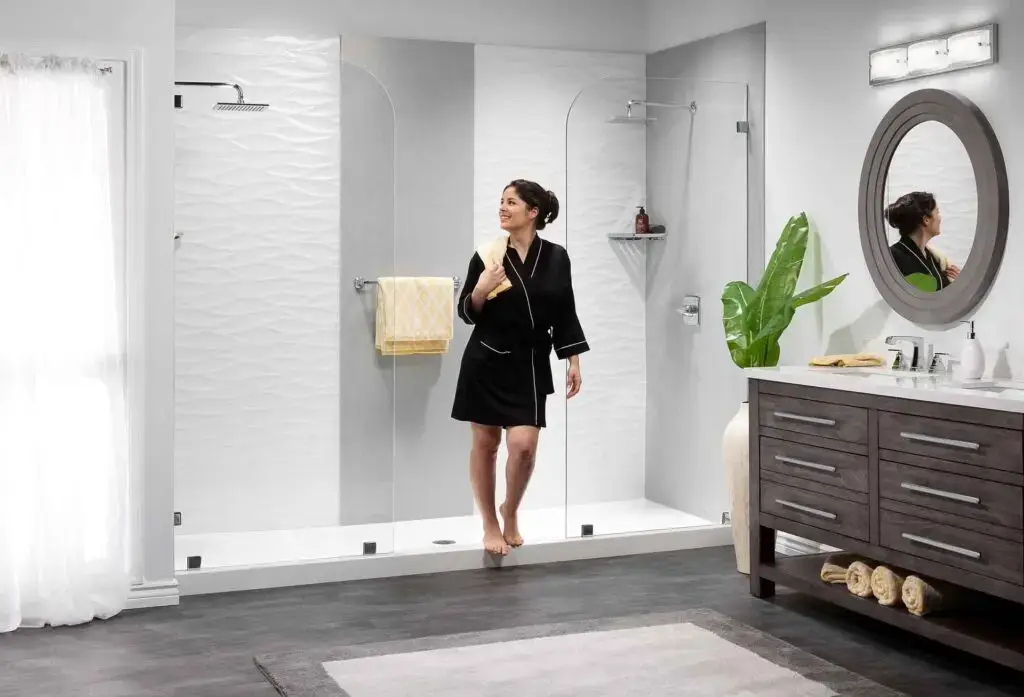 Modern frameless glass walk-in shower enclosure in a contemporary bathroom with textured wall tiles and double vanity.