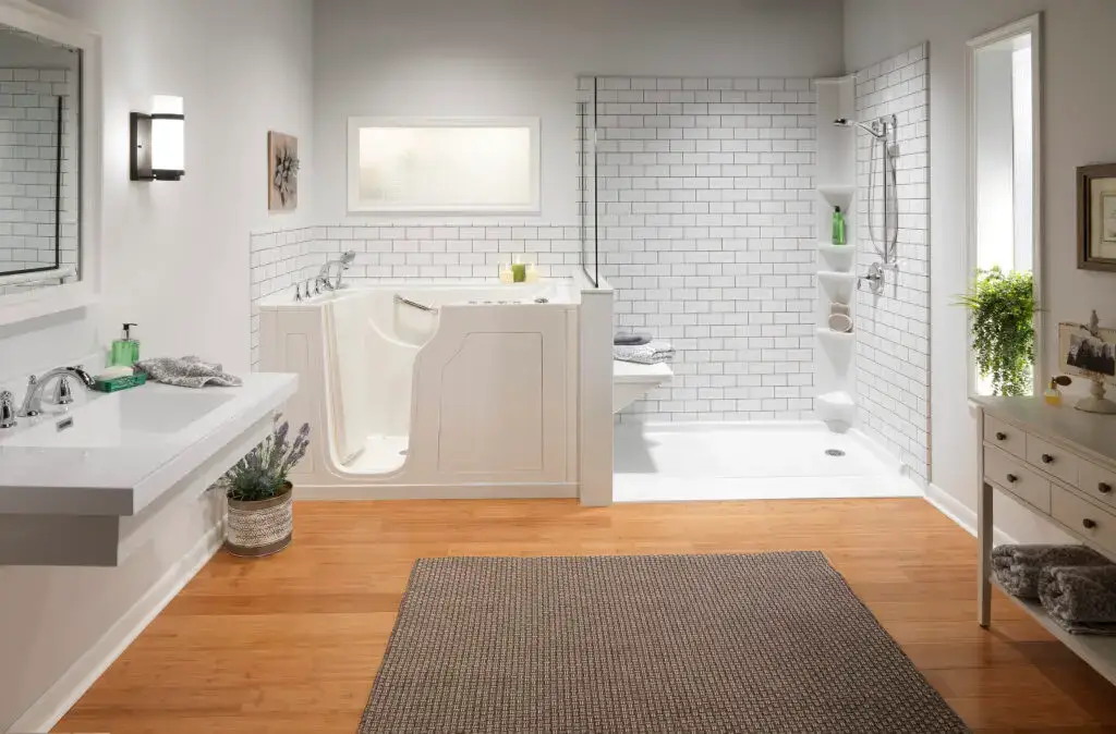 Spacious accessible bathroom layout featuring a white walk-in safety tub adjacent to a low-barrier walk-in shower with white subway tile walls, a built-in bench seat, and warm wood flooring.