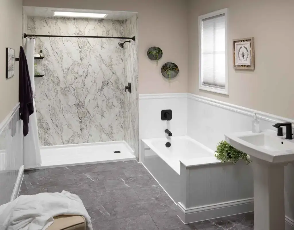 Complete bathroom renovation featuring a white alcove bathtub, terrazzo-patterned shower wall panels, a matte black sliding glass door frame, and a white single vanity.