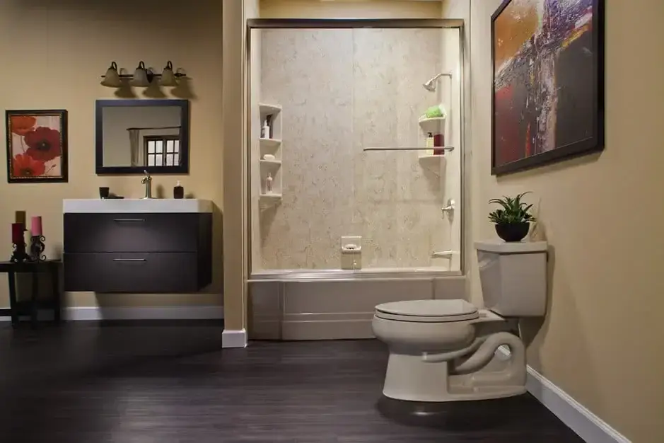 Bright master bathroom featuring an open-concept doorless walk-in shower with textured light grey stone walls, a white vanity with a black countertop, and an illuminated mirror.