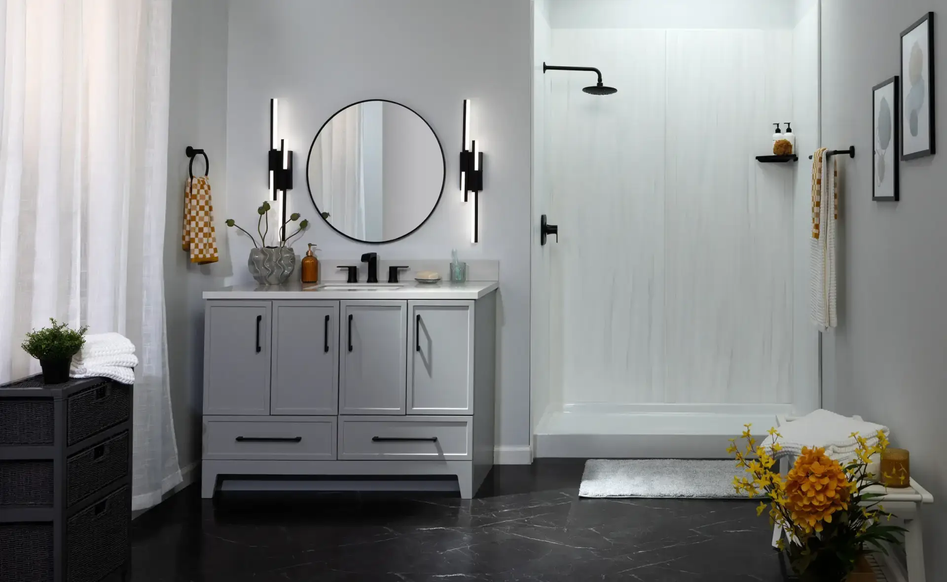 odern master bathroom featuring a grey single vanity with matte black hardware, a round mirror flanked by linear sconces, and a doorless walk-in shower on black marble-look flooring.
