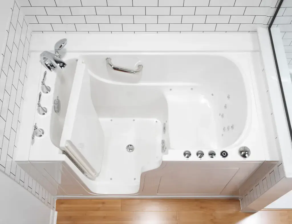 Top-down overhead view of a white walk-in safety bathtub showing the open inward-swinging door, integrated contour seat, hydrotherapy jets, chrome grab bar, and deck-mounted faucets.